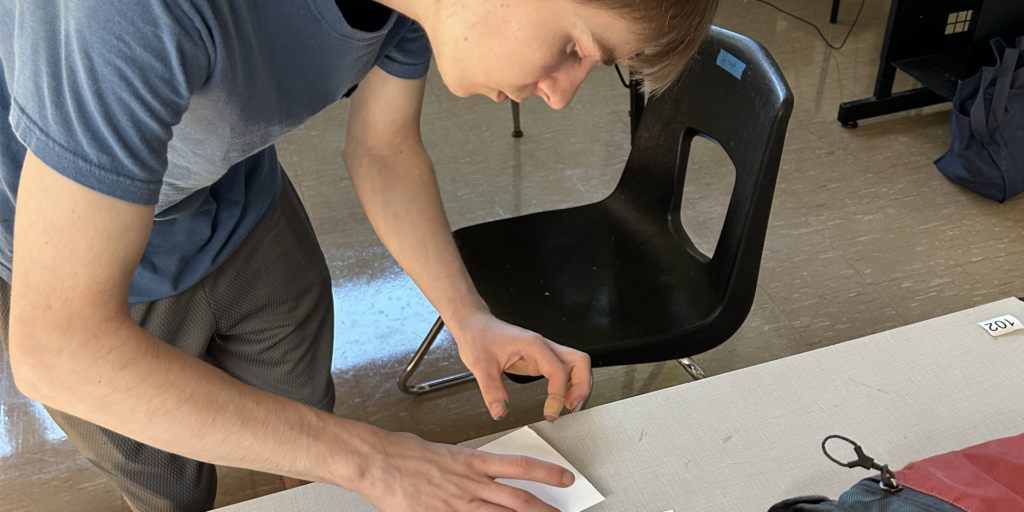 Student making a block print. Leaning close as he removes the paper from the block.
